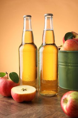 Cam şişelerde lezzetli elma şarabı ve ahşap masada portakal eğimli arka planda elmalar.