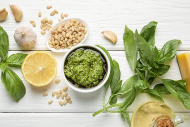 Tabakta taze pesto sosu ve beyaz ahşap masada malzemeler.