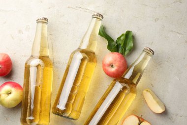 Cam şişelerde nefis elma şarabı ve gri desenli masada elmalar.