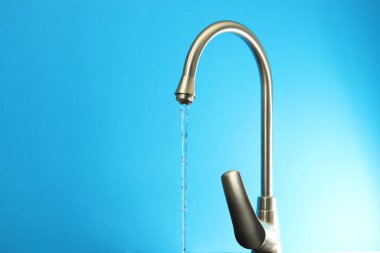 Su tasarrufu konsepti. Açık mavi arkaplandaki musluktan akan su akıntısı, yakın plan. Metin için boşluk