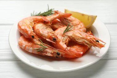 Beyaz ahşap masada biberiye ve limonla servis edilen lezzetli ızgara karidesler, yakın plan. Lezzetli deniz ürünleri yemeği.