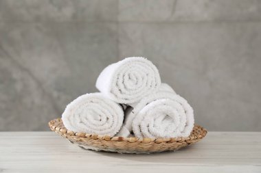 Hafif ahşap masada yuvarlanmış havlular gri duvara karşı, yakın plan.