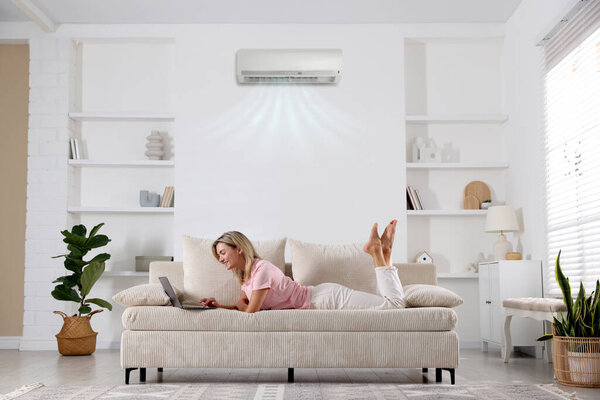 Woman using laptop on sofa in room with air conditioner