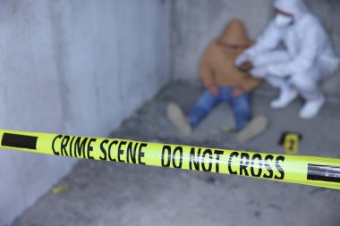 Adli tıp uzmanı terk edilmiş binanın içinde cesetle birlikte olay yerinde çalışıyor. Sarı polis bandına odaklan.