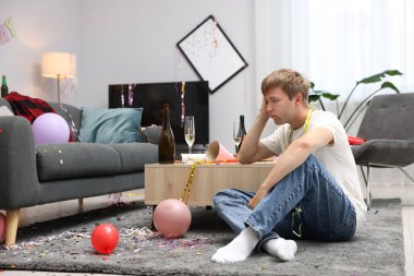 Adam partiden sonra dağınık bir odada akşamdan kalma halde yerde yatıyor.