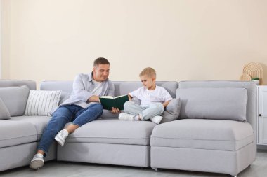Baba ve oğlu evdeki kanepede kitap okuyorlar.