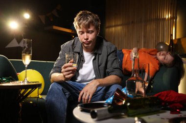 Bir bardak alkollü adam partiden sonra dağınık bir odada kanepede akşamdan kalma.