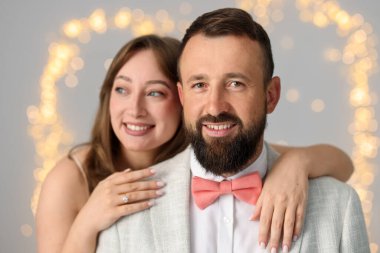 Evlilik teklifi yapıyor. Nişan yüzüklü kadın ve mutlu nişanlısı açık gri arka planda, bulanık ışıklarla sarılıyorlar.