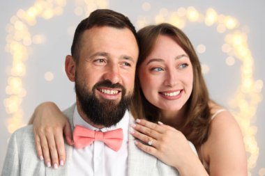 Evlilik teklifi yapıyor. Nişan yüzüklü kadın ve mutlu nişanlısı açık gri arka planda, bulanık ışıklarla sarılıyorlar.