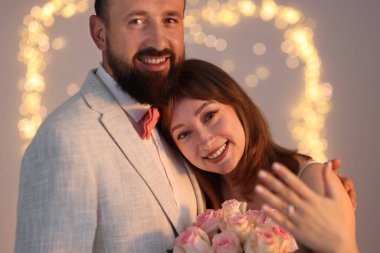 Evlilik teklifi yapıyor. Nişan yüzüklü bir kadın ve açık gri arka planda mutlu nişanlısı, bulanık ışıklar, bokeh etkisi.