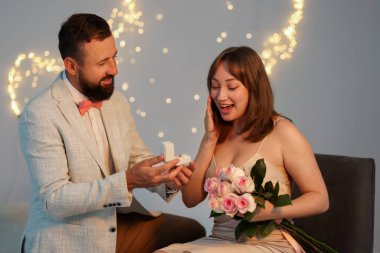 Nişan yüzüklü bir adam, açık gri arka planda, bulanık ışıklı, bokeh efektli kız arkadaşına evlenme teklif ediyor.