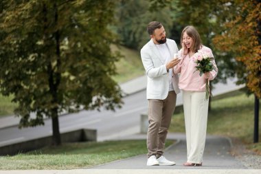 Nişan yüzüklü bir adam kız arkadaşına dışarıda evlenme teklif ediyor.