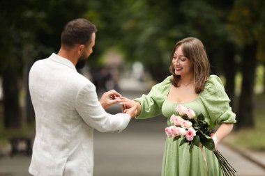 Evlilik teklifi yapıyor. Bir adam dışarıda kız arkadaşının parmağına nişan yüzüğü takıyor.