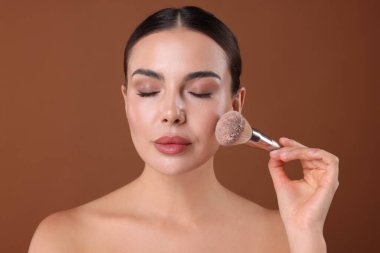 Güzel bir kadın kahverengi arka planda fırçayla makyaj yapıyor.