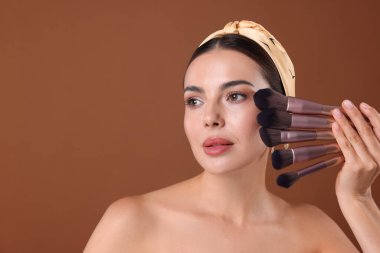 Kahverengi arkaplanda makyaj fırçası olan güzel bir kadın, metin için boşluk