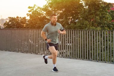 Spor giyimli atletik genç adam dışarıda koşuyor.