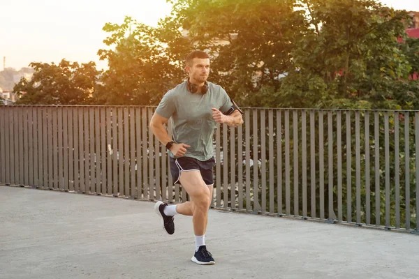 Spor giyimli atletik genç adam dışarıda koşuyor.