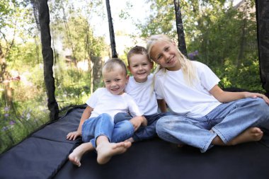 Dışarıda siyah trambolinde oturan mutlu çocuklar.