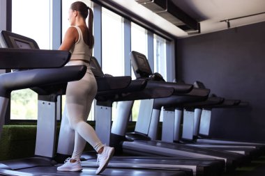 Spor salonunda koşu bandında antrenman yapan atletik bir kadın.