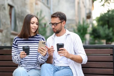 Paket kahve. Açık hava bankında kağıt bardaklar ve akıllı telefonlar olan bir çift.