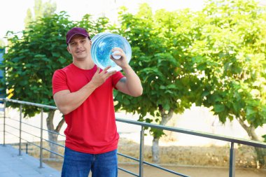 Parmaklıkların yanında serin su şişesiyle gülümseyen teslimatçı. Metin için boşluk