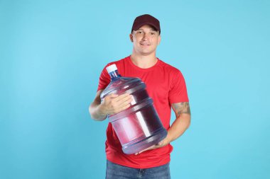 Açık mavi arka planda soğuk su şişesiyle gülümseyen teslimatçı.