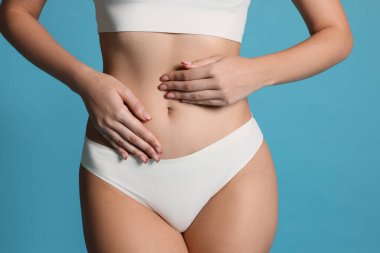 Açık mavi arka planda düz göbekli genç kadın, yakın plan.