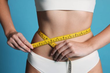 Düz karnını açık mavi arka planda bantla ölçen genç kadın, yakın plan.