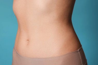 Açık mavi arka planda düz göbekli genç kadın, yakın plan.