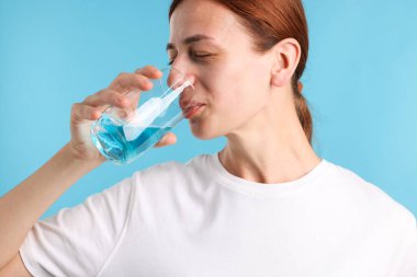 Açık mavi arka planda ağız gargarası olan bir kadın.