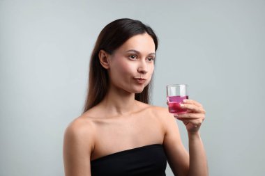 Gri arka planda ağız gargarası olan genç bir kadın. Ağız temizliği.