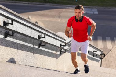 Spor kıyafetli bir adam merdivenlerden dışarı koşuyor.