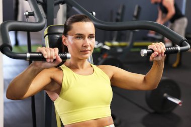 Spor salonunda omuz pres makinesi eğitimi alan atletik bir kadın.