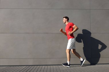 Spor giyimli bir adam binanın yanında koşuyor. Açık havada, mesaj için yer var.