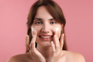 Güzel bir kadın pembe arka planda yüzüne krem sürüyor, yakın plan.