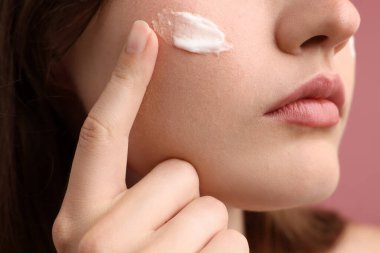 Pembe arka planda krem sürmüş güzel bir kadın, yakın plan.