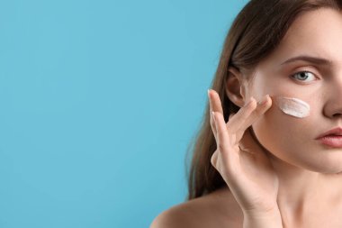 Yüzünde krem lekesi olan güzel bir kadın açık mavi arka planda, yakın plan. Metin için boşluk