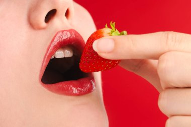 Güzel dudakları olan ve kırmızı arka planda çilekli bir kadın, yakın plan.