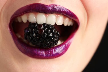 Güzel dudaklı kadın makyajı ve siyah arkaplanda böğürtlen, yakın plan.