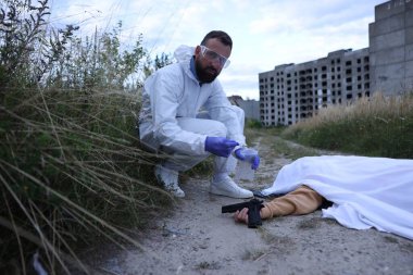 Adli tıp uzmanı dışarıda cesetle birlikte olay yerinde çalışıyor.