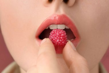 Güzel dudaklı, makyajlı ve ahududu şekerli bir kadın. Yakın plan.