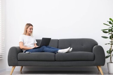 Evdeki kanepede dizüstü bilgisayarı olan kadın. Metin için boşluk
