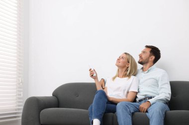 Evdeki kanepede klima kontrol etmek için uzaktan kumanda kullanan çift. Metin için boşluk