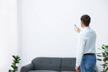 Evdeki klimayı uzaktan kumandayla kontrol eden bir adam. Metin için boşluk