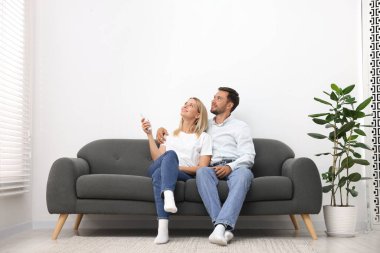 Evdeki koltukta uzaktan kumandayla klima kullanan çift.