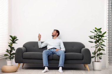 Evdeki kanepede uzaktan kumandayla klima kullanan bir adam.