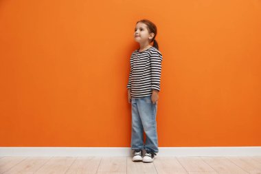 Turuncu duvarın yanında duran tatlı küçük kız.