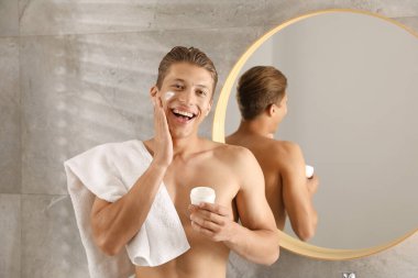 Yakışıklı genç adam banyoda yüzüne krem sürüyor.