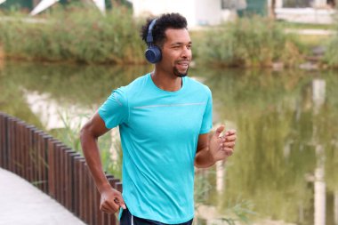 Nehir kenarında koşan kulaklıklı gülen adam.