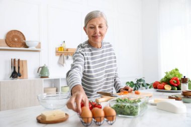 Üst düzey kadın mutfaktaki beyaz mermer masada yemek pişiriyor.